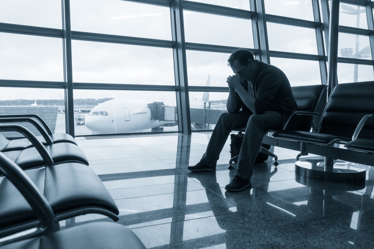 hombre sentado en sala de espera de aeropuerto con manos en la cara y situación de desesperación