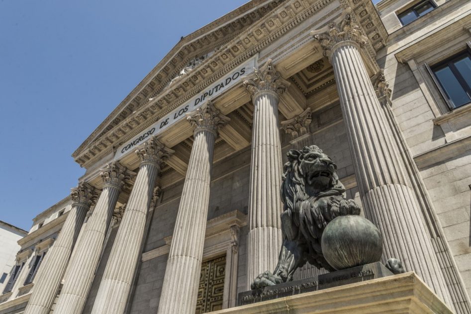 edificio de piedra emblemático del congreso de los diputados. león de bronce en un pedestal con la pata izquierda sobre una bola.