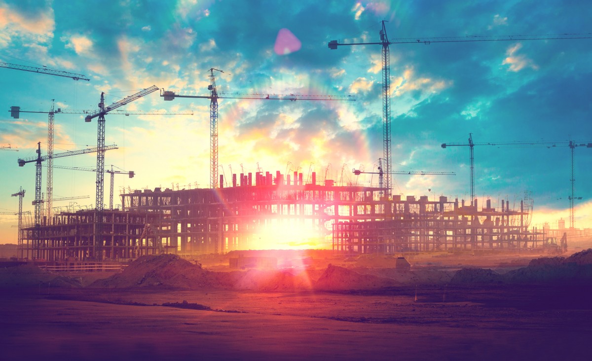 Cielo azul. Grúas en una construcción de pisos con resplandor del sol al atardecer.