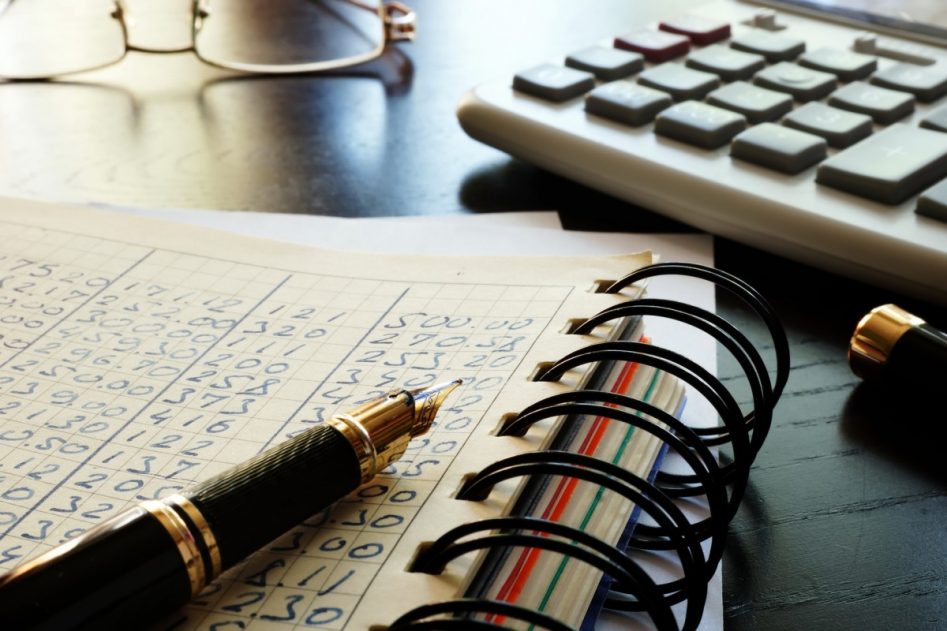 una pluma de escribir sobre agenda de contabilidad sobre una mesa y una calculadora. Gafas de ver al fondo