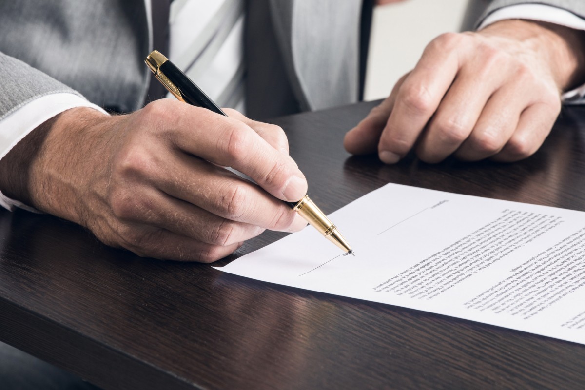 manos de hombre sobre documento encima de la mesa a punto de firmar un contrato
