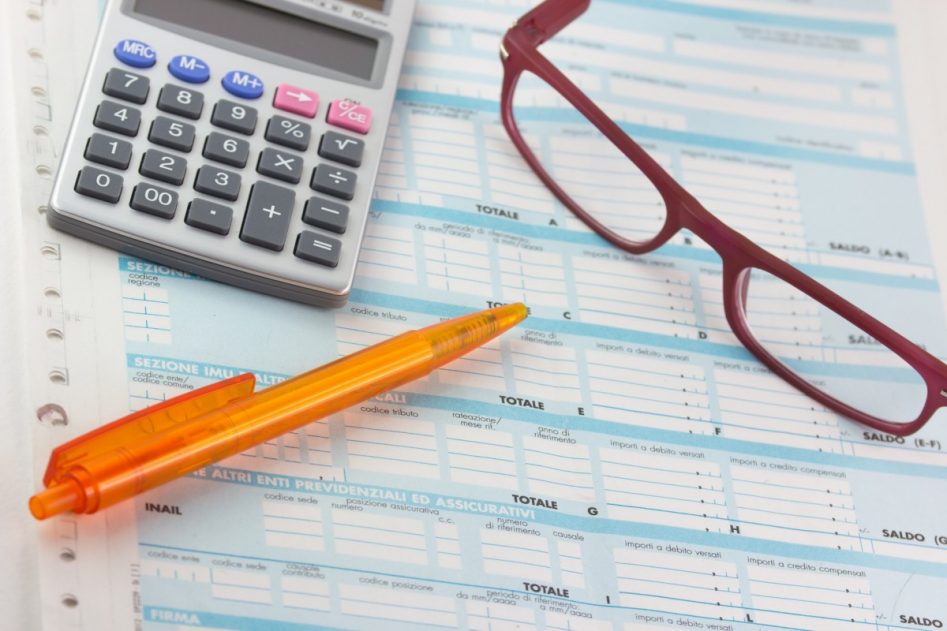 unas gafas rojas, un bolígrafo naranja y una calculadora sobre documentación