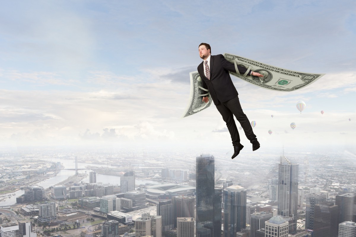 hombre volando con billetes por alas sobre ciudad de edificios.