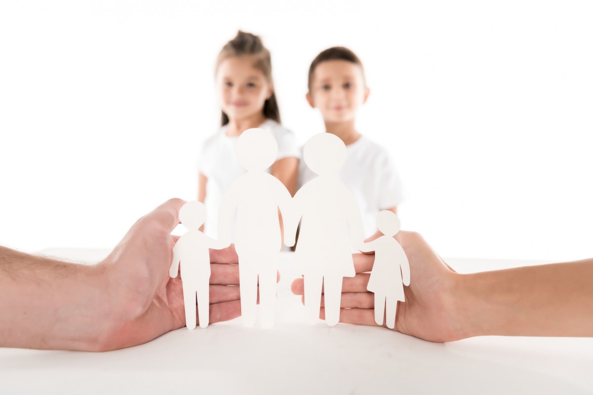 unas manos cubriendo figuras de papel blancas y dos niños al fondo