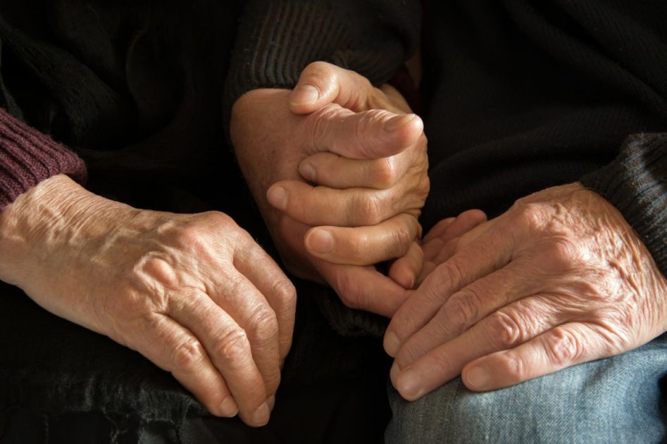 dos personas mayores se cogen de la mano mientras las apoyan en sus rodillas